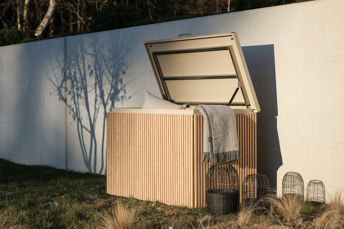 Cubic Box storage box with vertical iroko slats and the lid open against a concrete wall